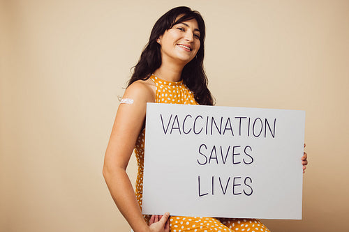 Beautiful woman holding "vaccination saves lives" signboard