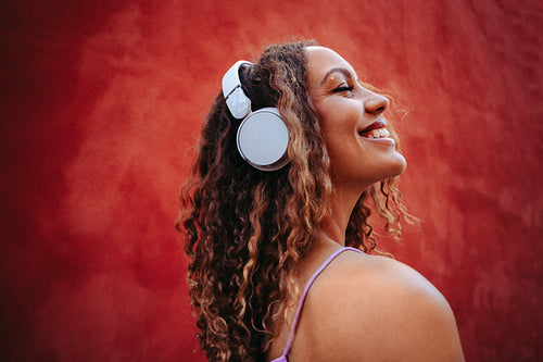 Woman enjoys music in headphones against red wall outdoors