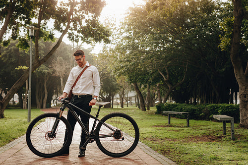 Smiling businessman standing in park with his bicycle