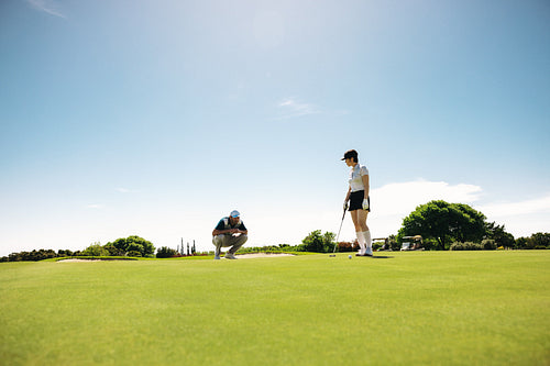 Female golfer in golf attire on putting green with male observer