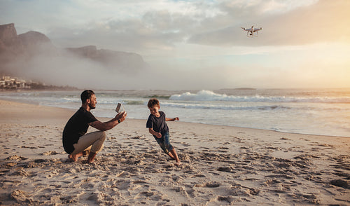 Father flying drone and son running on beach