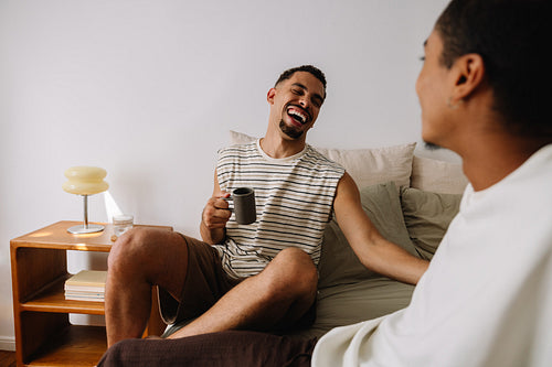 Young friends sharing a joyful moment and coffee in a cozy bedroom setting