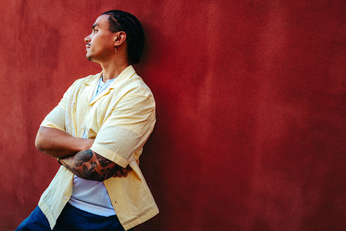 Man looks away while leaning against a red wall in the city