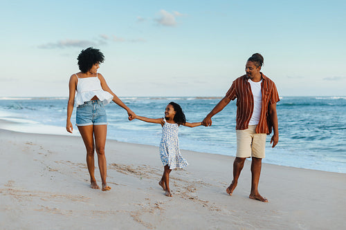 Happy family walking on the beach at sunset, holding hands and smiling.