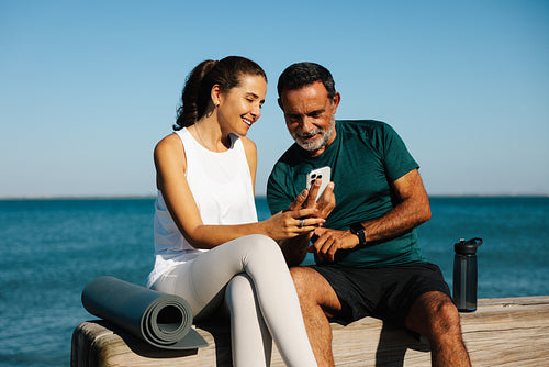 Two friends relaxing by the sea while viewing a phone together