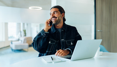 Man on phone in office with laptop and notebook
