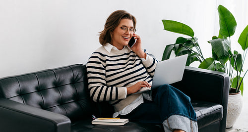 Woman multitasking with laptop and phone in a relaxed home setting