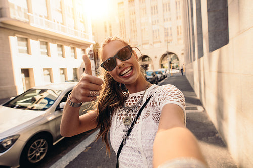 Tourist taking selfie in a street surrounded by buildings.
