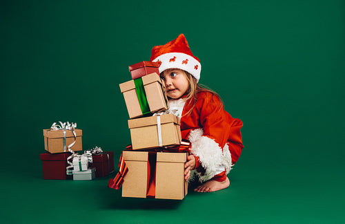 Kid dressed as santa lifting gift boxes