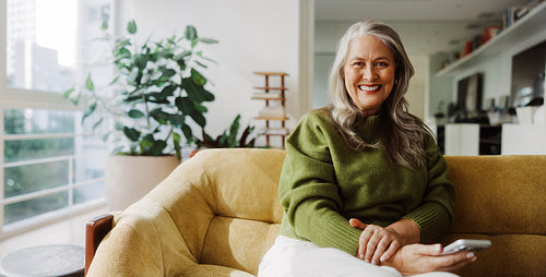 Seated senior woman uses a smartphone in the living room