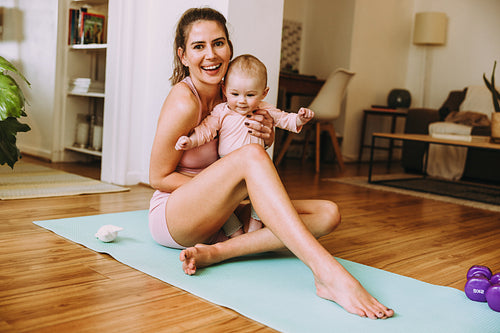 Smiling mom holding her baby while sitting on an exercise mat