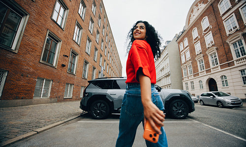 Woman walking to electric car charger while checking phone on city street