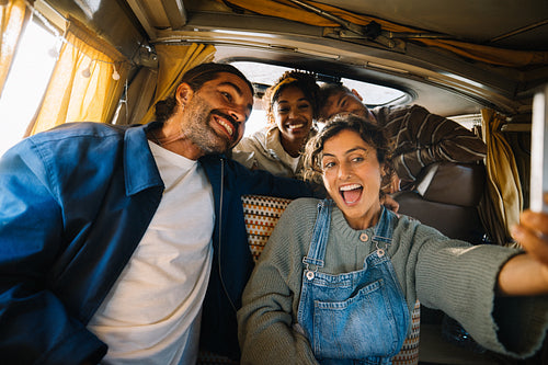Group of friends enjoy a fun road trip in a camper van and take a group selfie