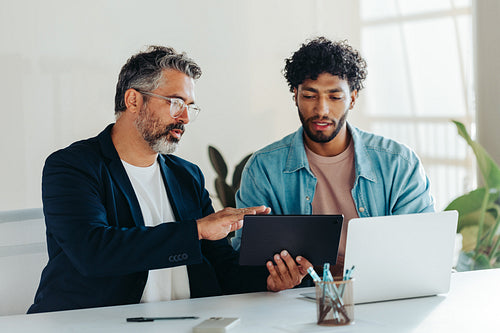Two professional men collaborating in modern office using tablet and laptop