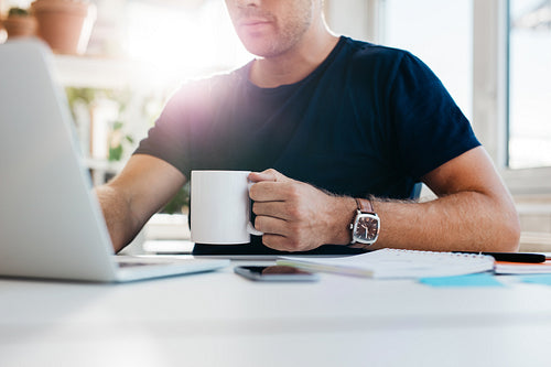 Young man with cup of coffee working on laptop