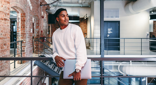 Young businessman standing with a laptop in a modern workplace