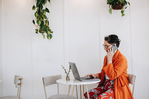 Business woman making a phone call and typing on a laptop while working in a cafe