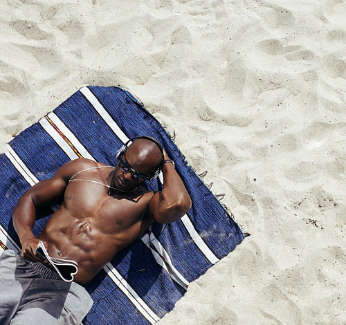 Muscular young man reading magazine on beach