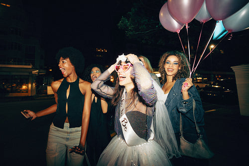 Excited group of friends celebrating bachelorette with balloons and festive attire outdoors