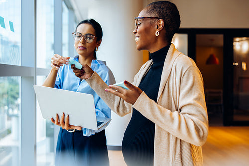 Two professionals discussing ideas with a laptop and sticky notes near the window