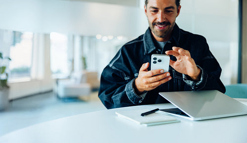 Man using phone at desk with laptop