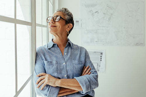 Thoughtful professional woman with silver hair looking outside a window in an office