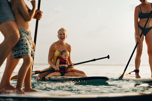 Mother and child paddleboarding with family during a sunny outdoor adventure