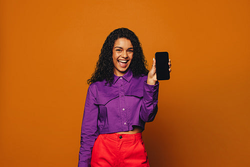 Cheerful woman smiling and recommending smartphone app on vibrant orange background