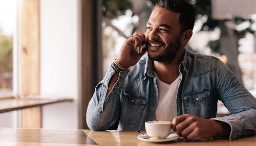 Young man in coffee shop talking on mobile phone