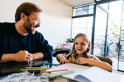 Father and daughter draw together at sunny kitchen table