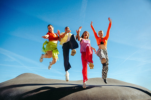 Friends leap joyfully together in outdoor celebration under blue sky