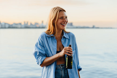 Blonde woman enjoying a sunset by the water with a beer