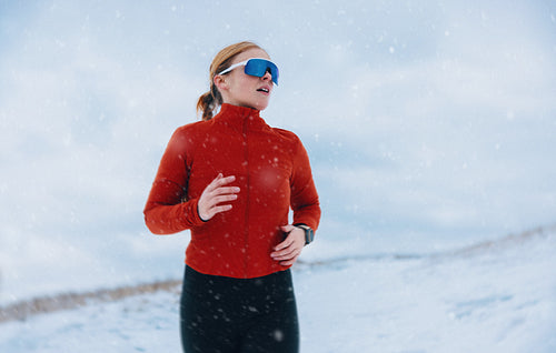 Determination defines the running woman in winter snow during outdoor fitness