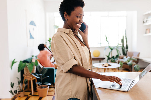 Black mature woman happily speaking on a mobile phone while working from home