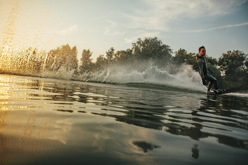 Wakeboarder skiing on lake at sunset