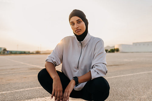 Muslim sportswoman looking at the camera while squatting outdoors