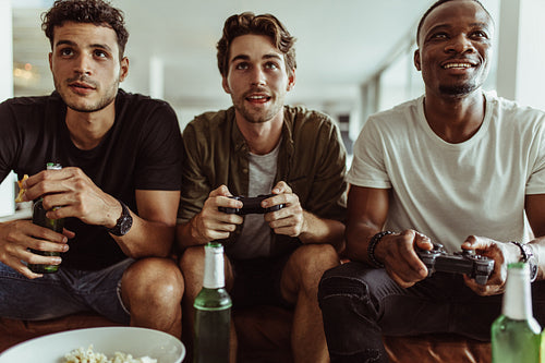 Three friends playing video game sitting at home