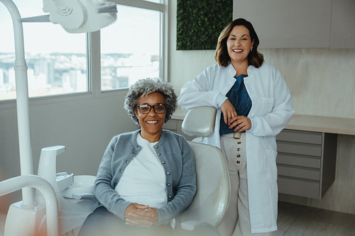 Female dentist smiles with senior patient in modern clinic