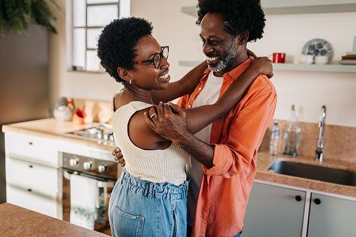 Happy husband and wife sharing a romantic embrace in their kitchen at home, enjoying their relationship