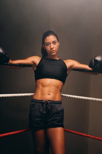 Young female boxer leaning against boxing ring ropes