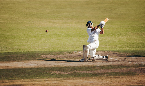 Professional male cricket player performing a powerful batting action in a match