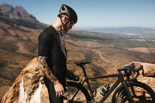Cyclist standing on mountain road with bike