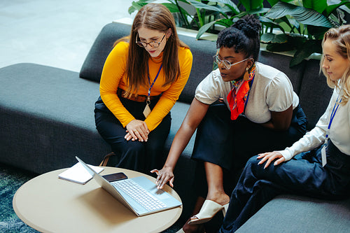 Three professional women collaborating on a laptop in a modern office