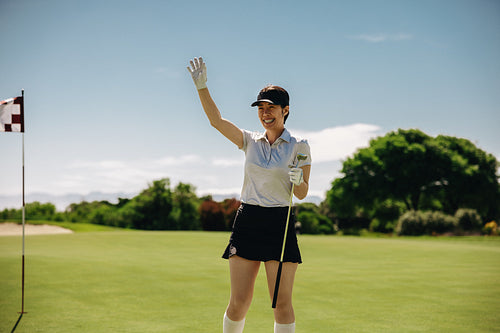 Smiling woman golfer happily waving on putting green