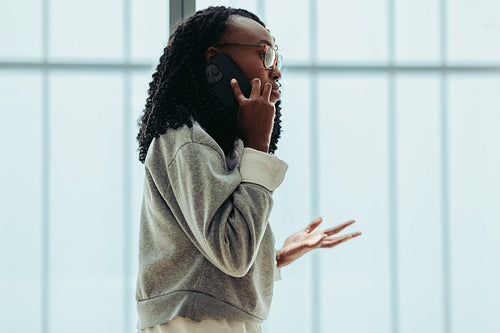 African female business professional talking on the phone with a client in a bright office setting