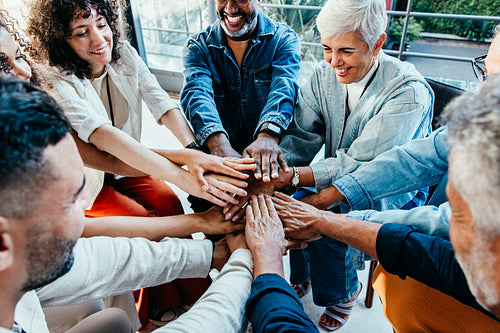Co-workers gathering together, hands in unity, smiling and bonding in a team-building activity.