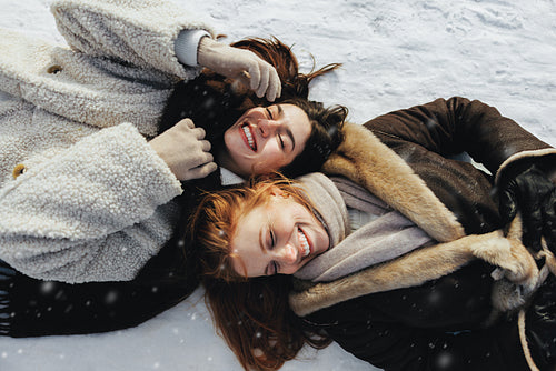 Women laugh together while lying in fresh snow