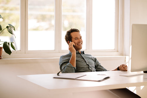 Entrepreneur talking on mobile phone while working on computer at home