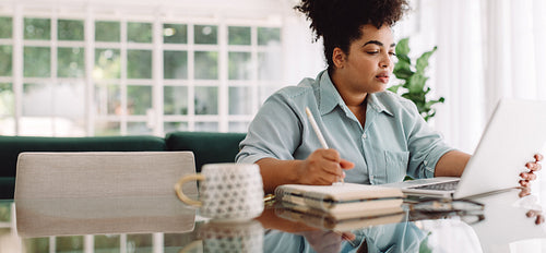 Businesswoman taking notes and using laptop at home