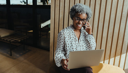 Mature businesswoman using laptop and smartphone in office lounge